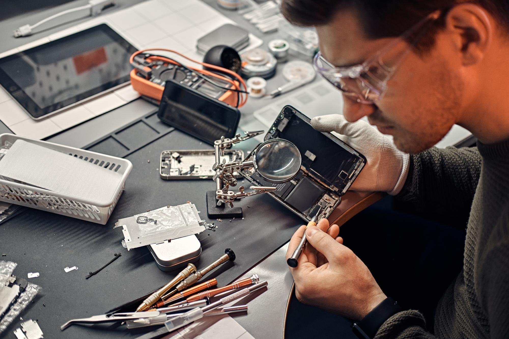 Técnico realizando reparo de um smartphone com lupa e ferramentas